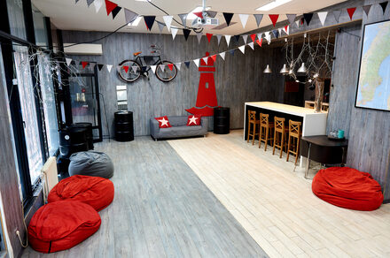 Стильный лофт в скандинавском стиле. Вход с улицы. Танцпол с красными пуфиками, красная елка на стене, гирлянды из флажков.