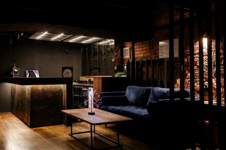 Treff8 Club (Трефф8 Клуб). Двухуровневый клуб под закрытие. Лофт-пространство с темными стенами и кирпичной кладкой. Деревянный пол, черный диван, деревянный стол. За стойкой темная кухня, металлические элементы. Слабое освещение, декоративный светильник на столе. Потолок с металлическими решетками.