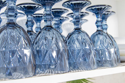 Лофт Облака. Зал Баунти на Сельскохозяйственной. Синий хрустальный бокал, перевёрнутый вверх дном, расположен на белой полке. Бокал с узором в виде геометрических форм. Поверхность полки частично покрыта текстурированной салфеткой. На заднем плане видны другие бокалы.