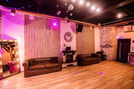 LoftForParty (ЛофтФорПати). Бэкстейдж лофт . Простор с деревянным полом и светлыми стенами, декорированными вертикальными панелями. Две коричневые кожаные софы, зеркало, настенное декоративное зеркало, несколько подвесных диско-шаров, сцена с DJ-аппаратурой, разноцветное освещение.