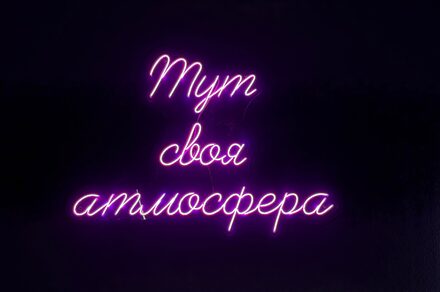 Лофт «Блэкберри». Неоновая надпись «Тут своя атмосфера» розового цвета на черном фоне.
