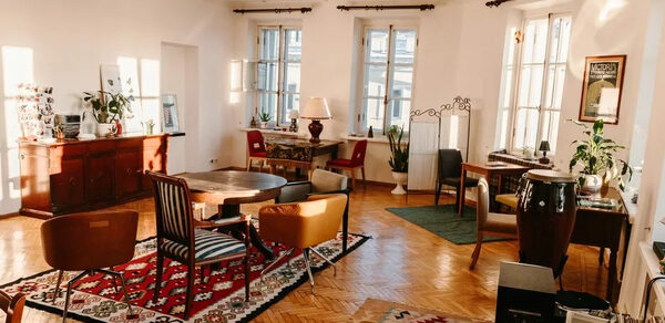 Светлый лофт с панорамным видом. Озарённое светом пространство. Столы со стульями. Ковры на полу. Различные элементы декора. Тумбочка