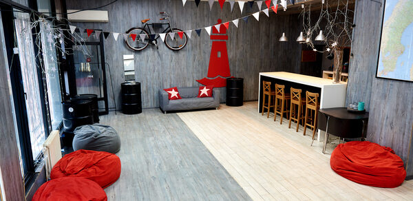 Стильный лофт в скандинавском стиле. Вход с улицы. Танцпол с красными пуфиками, красная елка на стене, гирлянды из флажков.