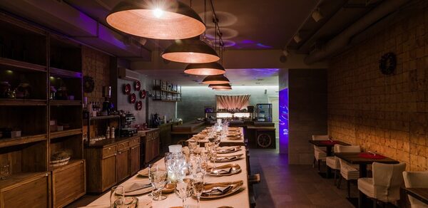 Нора. Оборудованный зал. Затемнённое освещение. Столы с сервировкой. Подвесные лампы. Небольшие столики "на двоих"