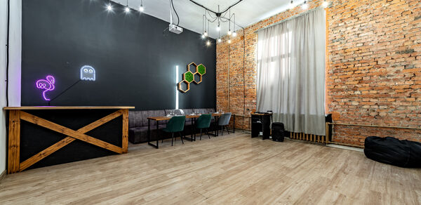 Rubin Loft (Рубин Лофт). Лофт средний. Лофт с деревянным полом, кирпичными стенами и черным потолком. Барная стойка, диван и стулья. Неоновая вывеска на стене. Подвесные светильники и светодиоды. Легкие шторы на окне. Декор в виде сот. Черные мешки для сидения.