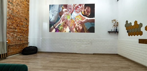 Rubin Loft (Рубин Лофт). Лофт средний. Лофт-пространство с кирпичной стеной и белыми панелями, подвесное освещение, деревянный пол, зелёный стул, черный пуф, проектор изображение на стене, полка с декором, настенные деревянные соты.