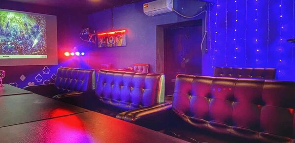 Rave(Рейв). Караоке-зал с диванами из коричневой кожи, темными деревянными столами и синим подсвеченным фоном. На стене проектор и гирлянда из огней. Настенное кондиционирование, неоновая вывеска, декорации в виде карт.