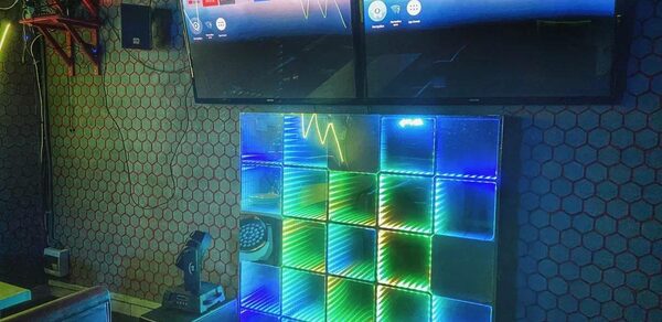 Bee-lounge(Пчела-лаундж). Караоке-зал с двумя настенными экранами, светодиодная панель с разноцветной подсветкой. Обои с геометрическим узором, потолочные коммуникации, колонки. Мягкие стулья, приглушенное освещение.