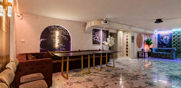 Стильный лофт Джаванди. Современное пространство с мраморным полом и светлыми стенами. Комплектация включает длинный стол с золотистыми ножками, диваны, стулья. Освещение разноцветное, неоновое, с декоративными панелями на стенах. Декор включает искусственные цветы и картины.