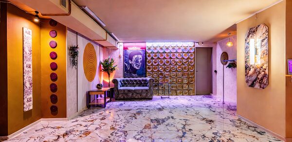 Стильный лофт Джаванди. Пространство с мраморным полом, светлыми стенами и подвесным потолком. Элементы декора: постеры, круглые панели, неоновая вывеска. Мебель: диван, столик, кресло. Освещение: встроенные светильники, неон. Стены украшены растениями.