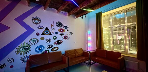 Яркий двухуровневый лофт. Приглушённый свет. Диваны. Стена с рисунками. Окно со светящейся гирляндой
