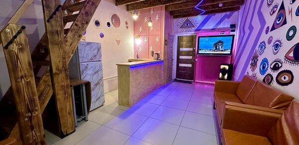 Яркий двухуровневый лофт. Барная стойка. Холодильник. Разноцветные украшенные стены. Диваны. Телевизор. Лестница на второй этаж