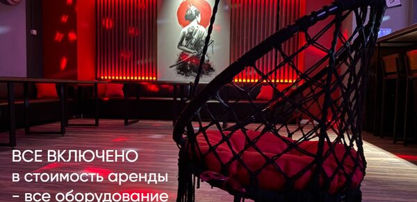 Лофт ИЗНАНКА. Зал ТОКИО. Пространство с подвесным креслом, креслом-мешком, столами вдоль стены, которое украшает картина. Настенный декор с подсветкой. Красные неоновые элементы освещения. Текст: «Все включено в стоимость аренды - все оборудование - инфраструктура».