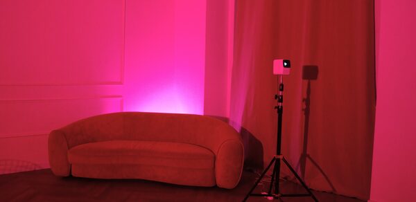 Стильный лофт для уютных вечеринок. Розовая подсветка, диван полукруглой формы, паркетный пол, шторы, стена с декоративными панелями, штатив с проектором, минималистичный интерьер, текстурированные материалы, отсутствие текстов и знаков.