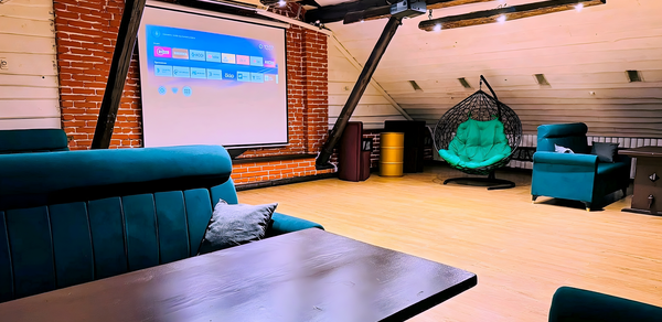 Лофт-мансарда . Лофт-пространство с кирпичными и деревянными стенами, светлым полом. Убедительные стулья и столы, подвесные светильники, экран проектора. Подвесное кресло, диваны зеленого и бирюзового цвета, деревянные балки на потолке.