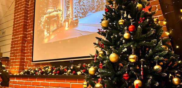 Двухуровневый Лофт с балкончиком. Новогодняя елка с золотыми и красными шарами на фоне кирпичной стены. Справа гирлянда из огоньков, слева проекция зимнего пейзажа с камином. Декорации из зеленых веток и шаров на выступе стены.