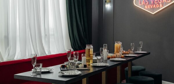 Rubin Loft (Рубин Лофт). Лофт Вегас. Длинный черный стол с сервировкой, высоким стеклянным графином, бокалами и закусками, окружен черными пуфами. Темные стены с неоновой надписью "Welcome to Fabulous Las Vegas Nevada". Белые и темно-зеленые шторы. Красные сиденья вдоль стены.