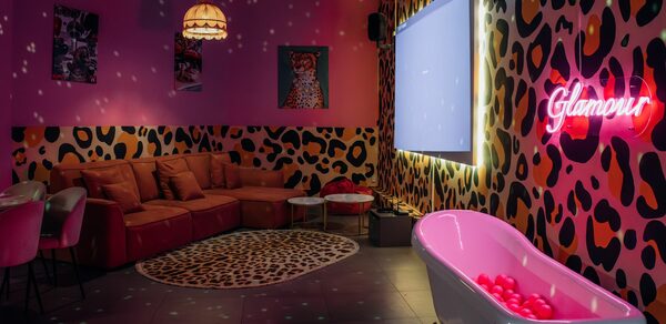 Rubin Loft (Рубин Лофт). Лофт Гламур. Караоке-комната с леопардовым принтом на стенах, красный угловой диван, круглые стулья, столы, экран, неоновая надпись "Glamour", ванна с розовыми шарами, висячая лампа, коврик с узором. Теплое освещение, тёмные потолочные конструкции.