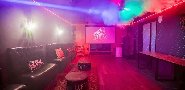 Пространство для любых мероприятий с верандой и грилем. Караоке-зал с приглушенным освещением, диванами черного цвета вдоль стены, пуфами, большим экраном для проектора. Деревянный пол, ковровое покрытие, стол вдоль правой стены. Светодиодные ленты на потолке, декоративные элементы на стенах.