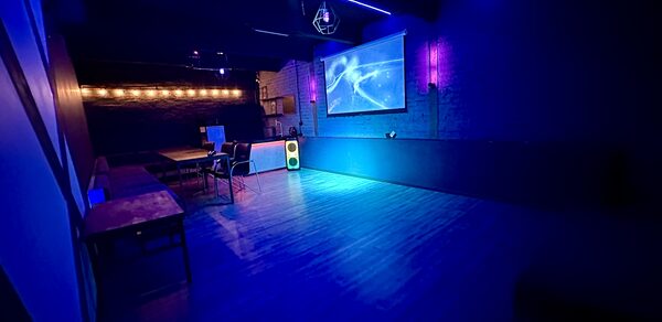 Kahovka loft (Каховка Лофт). Неоновый лофт-зал. Тёмное закрытое помещение с деревянным полом, напоминающее клуб или бар. На стене большой экран с проекцией, в комнате неоновая подсветка и диско-шар. Несколько столов и стульев у стены, светящаяся колонка.