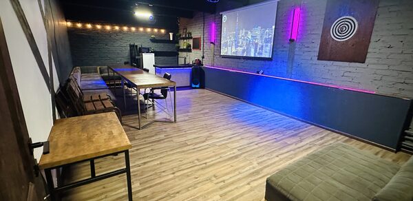 Kahovka loft (Каховка Лофт). Неоновый лофт-зал. Коворкинг-пространство с деревянным полом, кирпичными стенами серого цвета, длинным деревянным столом и креслами вдоль стены. Присутствует проектор, экран, атмосферное освещение, барная стойка и оригинальное настенное панно.