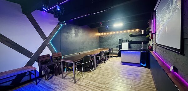 Kahovka loft (Каховка Лофт). Неоновый лофт-зал. Современное пространство с деревянным полом, стены отделаны черными и белыми панелями, потолок черный. Ряды стульев и столов, барная стойка, большой экран. Светодиодная и неоновая подсветка, гирлянды.