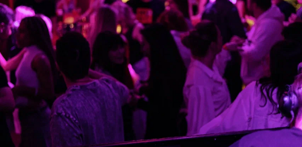 Бар StereoPeople (СтереоПипл). Танцевальная площадка с диджейским пультом на переднем плане. Люди танцуют и общаются в помещении с фиолетовым и розовым освещением. Интенсивное использование цветов создает вечернюю атмосферу.