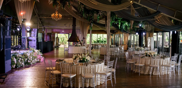 Soho Country Club (Сохо Кантри Клаб). Банкетный зал с деревянным полом и высоким потолком, декорирован тканями и зеленью. Круглые столы с бежевыми скатертями и прозрачными стульями. В центре люстры, сцена с музыкальной аппаратурой и цветами, витражные окна, освещение с оттенками розового и зелёного.