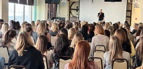 Зал 9. Просторный конференц-зал до 200 человек в Академии Кантаты. Конференц-зал с белыми стенами и окнами с защитными шторами. Размещение стульев в рядах; организатор на сцене с микрофоном. Потолочные динамики, светильники и подвесные экраны. Светлые стены, ковровое покрытие.