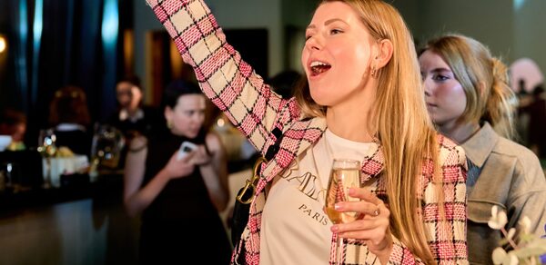 Лофт для мероприятий с гольф-симулятором. Группа людей, одетых в современную одежду, находятся в помещении с барной стойкой. Освещение тёплое, присутствуют элементы декора. Один человек держит бокал. Цветовая гамма включает тёмные и светло-зелёные оттенки.