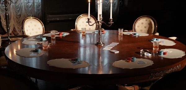 Polygon(Полигон). Зал Апартаменты. Круглый деревянный стол с резными деталями, окружён шестью стульями с белой обивкой. На столе игральные карты, фишки и стаканы с напитками. В центре подсвечник с зажженными свечами. На заднем плане тёмная занавеска и фортепиано. Освещение тусклое.