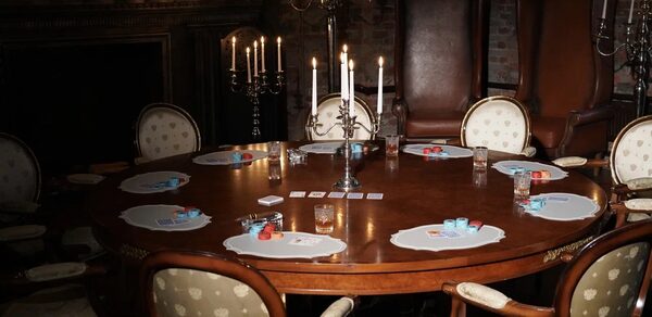 Polygon(Полигон). Зал Апартаменты. Круглый деревянный стол с расставленными вокруг стульями, на столе карточные наборы и стаканы. Центральная композиция из свечей на подсвечниках. Низкое освещение, стены из кирпича.