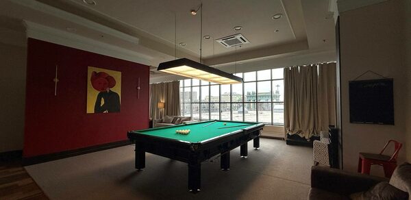 Студия Н. Бильярдная комната с зеленым столом, висячей лампой над ним, большим окном с занавесками. На стене висит картина. На полу ковровое покрытие, по бокам диван и кресло, справа красный стул. Потолочное освещение и встроенная система кондиционирования.