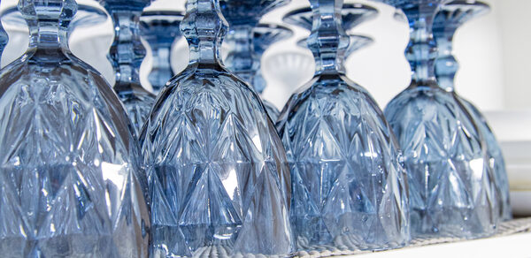 Лофт Облака. Зал Баунти на Сельскохозяйственной. Синий хрустальный бокал, перевёрнутый вверх дном, расположен на белой полке. Бокал с узором в виде геометрических форм. Поверхность полки частично покрыта текстурированной салфеткой. На заднем плане видны другие бокалы.