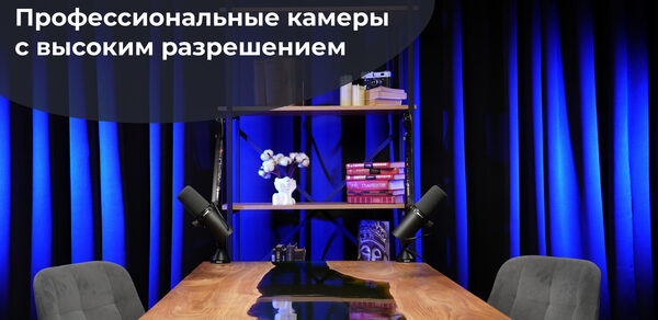 Лофт Восторг. Современное пространство с деревянным столом и серыми стульями. На столе черные микрофоны. Позади полка с книгами и декором, включая цветы. Задник оформлен темными шторами с синим освещением. Текст «Картинка 4К: Профессиональные камеры с высоким разрешением».