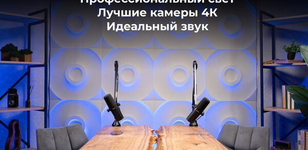 Лофт  Эйфория. Пространство с деревянным столом и двумя микрофонами на стойках. Стена с геометрическим узором и подсветкой. Серые кресла по бокам стола. Полки с книгами и декоративными элементами по бокам. Текст на стене на русском языке.