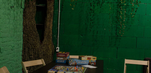 Хендмейдщики. Лофт в лесной тематике. Зал с зелёными кирпичными стенами, декорацией в виде ствола дерева и висящей листвой. Чёрный стол с настольными играми и карточками. Деревянные стулья. Освещение уютное и приглушённое, розетка на стене.