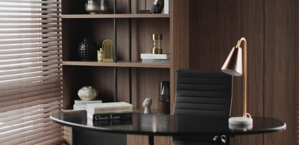 Mimika(Мимика). Просторная фотостудия. Офисное пространство с овальным столом из темного дерева, черным кожаным креслом, лампой с медным абажуром. Фоном служит деревянный стеллаж с книгами и декором. Слева жалюзи на окне, пропускающие свет. Цвета: коричневый, черный, медный.