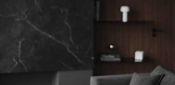 Mimika(Мимика). Просторная фотостудия. Современное пространство с темной мраморной отделкой стены, серым диваном, стеклянными бокалами на столе. Деревянная стена-панель с открытыми полками, на которых размещены книги и белый декор. Мягкое освещение, минималистичный стиль.