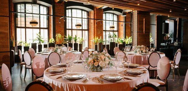 Zafferano Loft(Зафферано лофт). Просторное помещение с крупными арочными окнами и кирпичными стенами. Несколько круглых столов сервированы посудой и цветочными композициями. Стулья с обитыми спинками. Потолок с деревянными рейками и подвесным освещением. Растения вдоль окон.