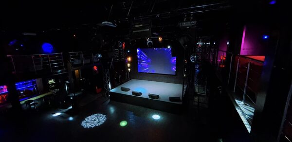 Castle Concert Hall(Концертный зал Замок). Темное пространство с большой сценой, экраном и разноцветными световыми эффектами. Металлические перила и конструкции, отражающие поверхности. На стенах подсветка красного и синего цветов. Светящиеся кружки на полу. Балконы и лестницы по краям.