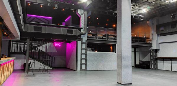 PRAVDA(Правда). Просторный зал на 800 гостей. Большое закрытое пространство с бетонным полом и высокими потолками, многоуровневое с лестницей, балкон. Есть знак "WC" с неоновой подсветкой, освещение в виде точечных светильников. Стены серые, чёрные деревянные и металлические элементы.