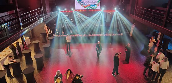 СВОБОДА. Зал на 1200 человек. Многоуровневое пространство с деревянным полом, окруженное перилами. В центре люди, по периметру высокие столы с черными скатертями. На сцене сзади стоит экран, над которым проецируется свет. Освещение яркое, цветное.