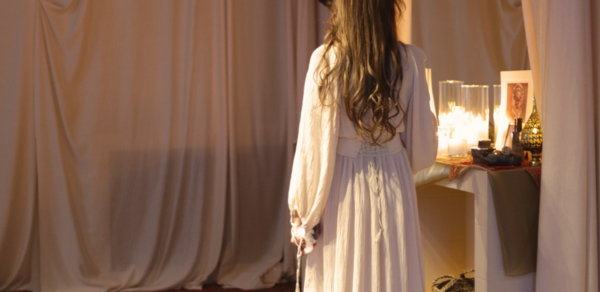 Лофт Поле. Уютный зал для мероприятий. Текстильное пространство с навесными тканями, журнальный столик с зажженными свечами и декором, штативная лампа, мягкие ковры с восточными узорами, светлая одежда человека, мягкое освещение.