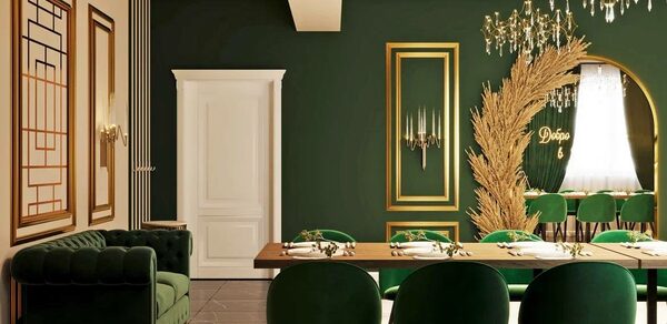 Голливуд. Элегантный лофт в зелено-бежевых оттенках. Зал с темно-зелеными стенами и белым потолком, длинный деревянный стол с зелеными стульями, рядом темно-зеленый диван. На стене декоративные элементы золотого цвета, светильник, золотистая композиция. Потолок украшен светильником-кристаллом.