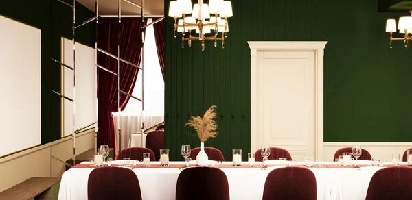 Вегас. Атмосферный лофт с акцентным дизайном. Уютное праздничное пространство с обеденным столом, покрытым белой скатертью, и бордовыми стульями. Потолочный светильник. Тёмно-зелёные стены, белая дверь и молдинги. Красные занавески на окнах. На стене панели и зеркальные элементы.