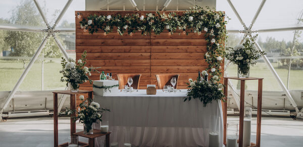 Эко-отель "Джао Да!Ча". Шатер-Сфера. Купольное пространство с панорамными окнами. Деревянная панель с зеленью. Стол с белой скатертью, украшенный цветами и свечами. Два стула. Деревянные стоянья с цветами. Пол серый. Натуральные материалы, нежные цвета.