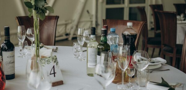 Эко-отель "Джао Да!Ча". Шатер-Сфера. Круглый стол, покрытый белой скатертью, сервирован бокалами и бутылками напитков, включая вино и газировку. На столе декоративная композиция из зелени и карточка с номером 4. Вокруг деревянные стулья.