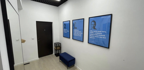 Уютный тренинговый зал на Таганской. Узкий коридор с белыми стенами, черным потолком с решеткой, деревянный пол. Черная дверь, три синих постера в рамках на стене, синий пуф, черный металлический фонарь. Светодиодные потолочные светильники.