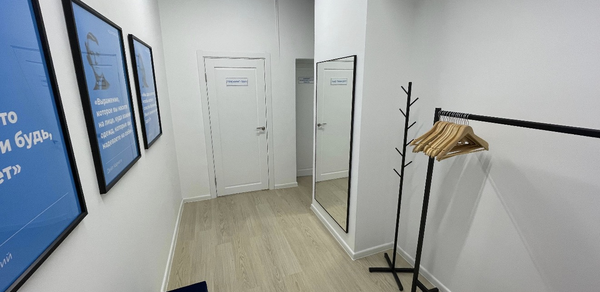 Уютный тренинговый зал на Таганской. Узкое светлое помещение с белыми стенами и светлым деревянным полом. Вдоль левой стены три синих постера в рамках. Справа зеркало и вешалка с плечиками. Потолок черный решетчатый. Две белые двери. На вешалке шесть деревянных плечиков.